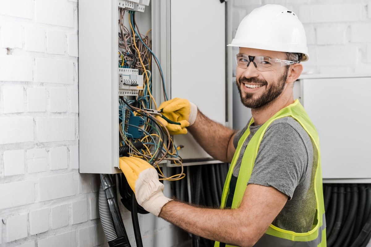 Smiling professional electrician repairing electrical panel in home
